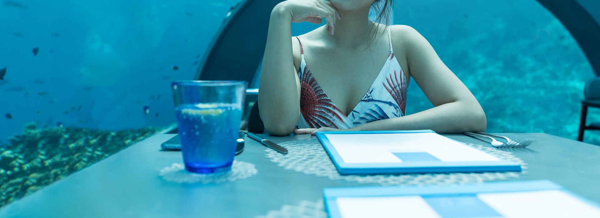 Una giovane donna sorridente seduta a un tavolo in un lussuoso ristorante sottomarino circondata dalla vita marina.