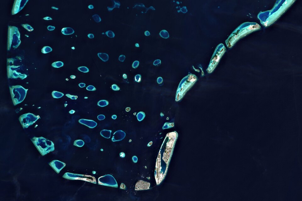 Vista satellitare ad alta quota che mostra le formazioni naturali di atolli corallini circondate da acque blu.